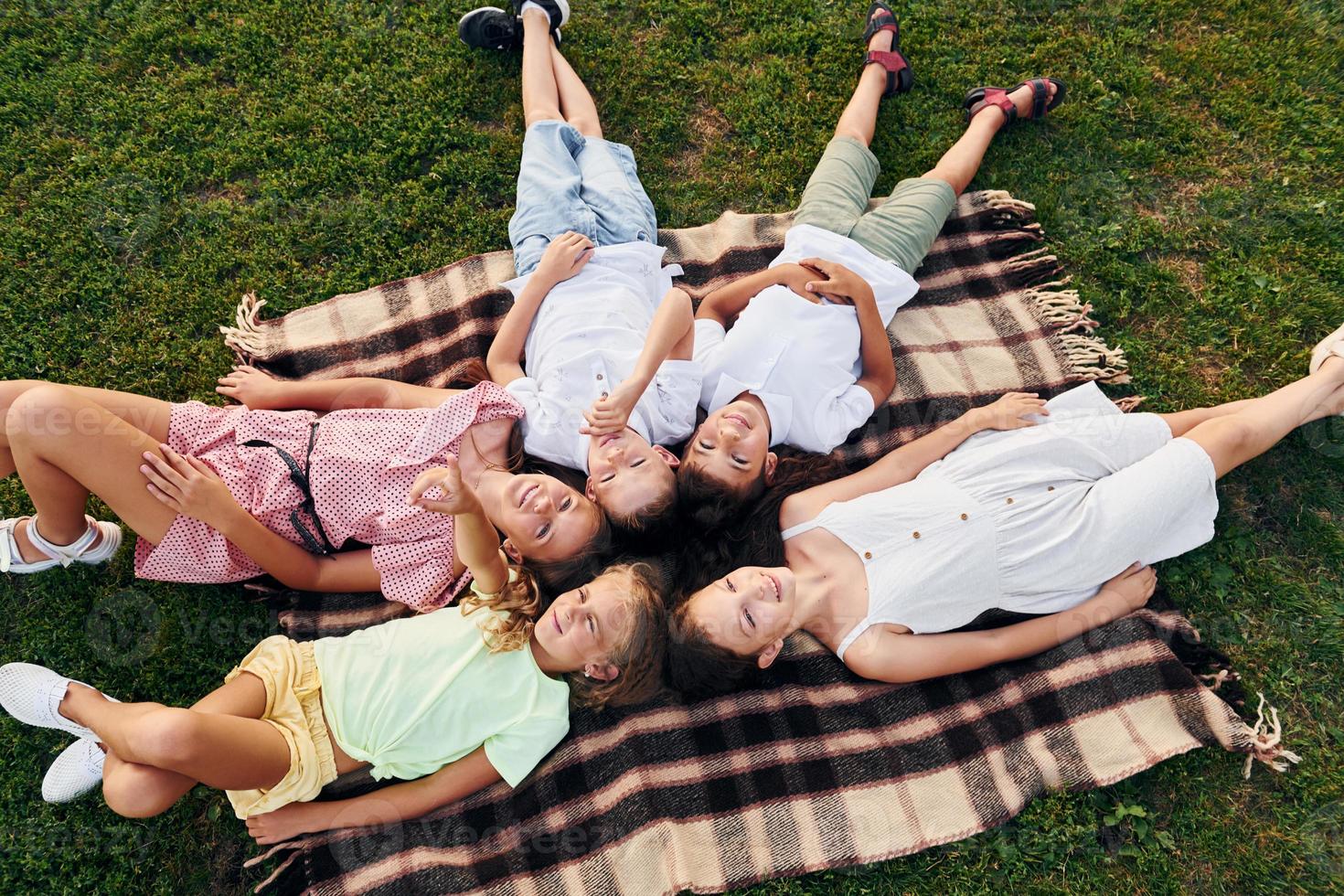 Having a rest and laying down. Group of happy kids is outdoors on the sportive field at daytime photo