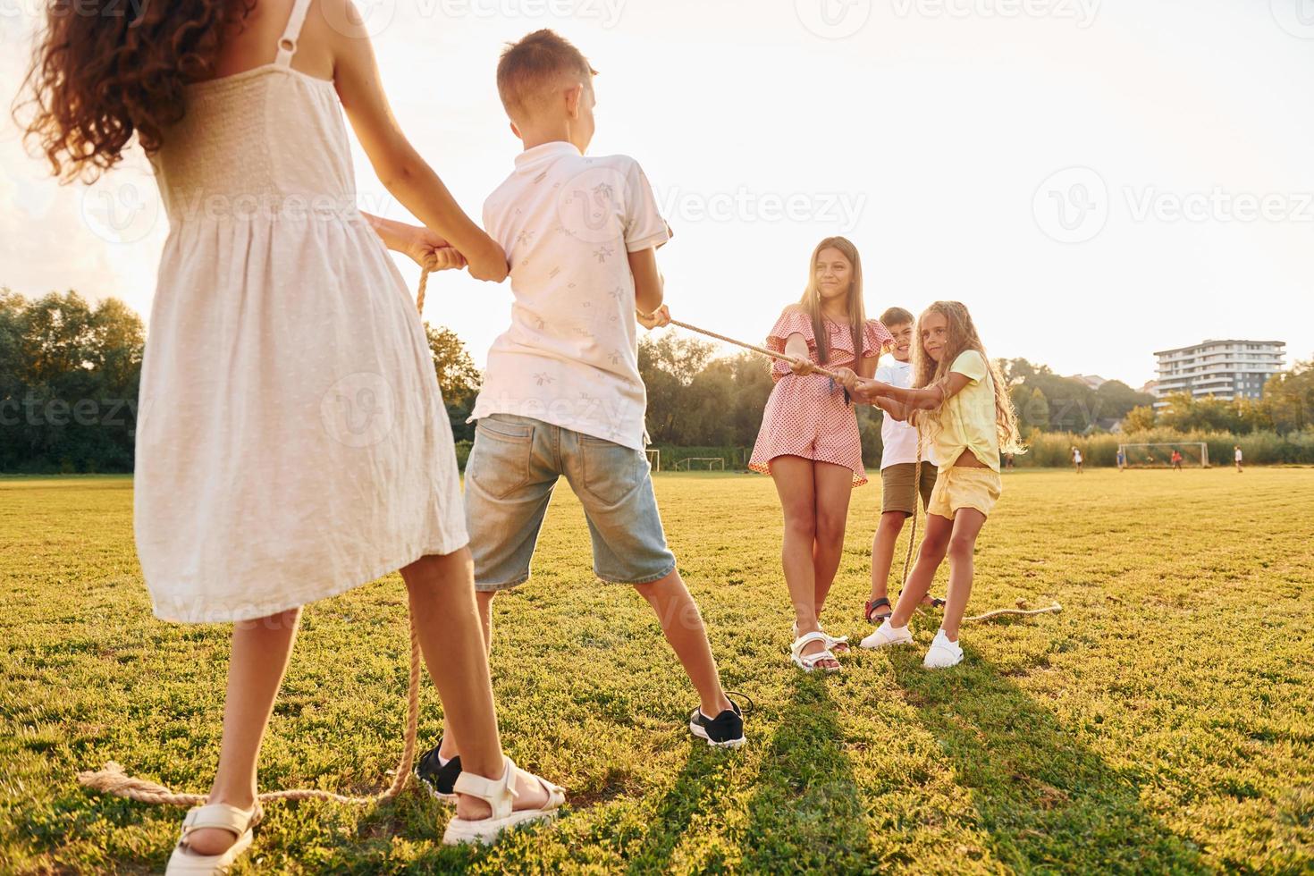 Playing tug of war. Group of happy kids is outdoors on the sportive field at daytime photo