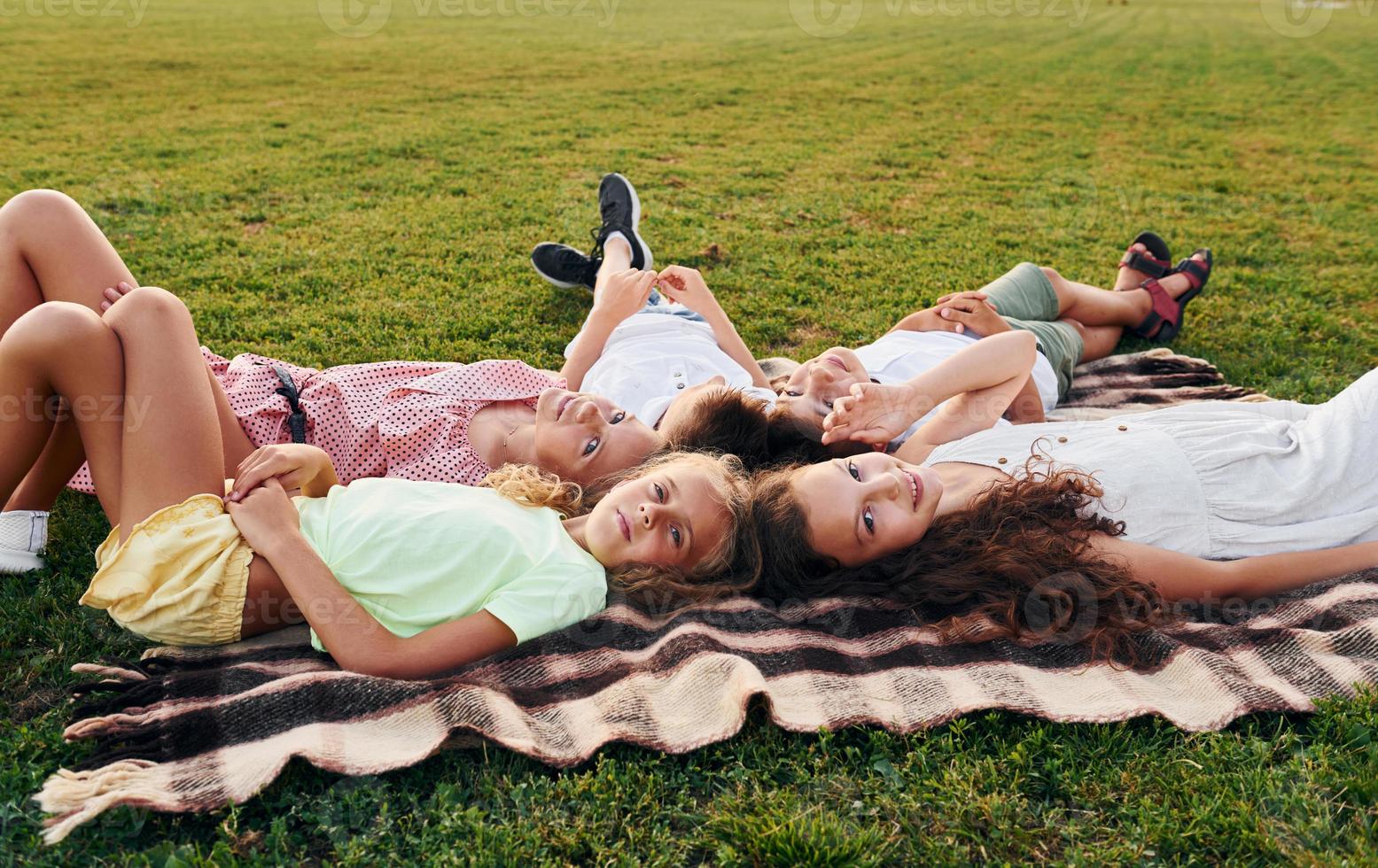Having a rest and laying down. Group of happy kids is outdoors on the sportive field at daytime photo