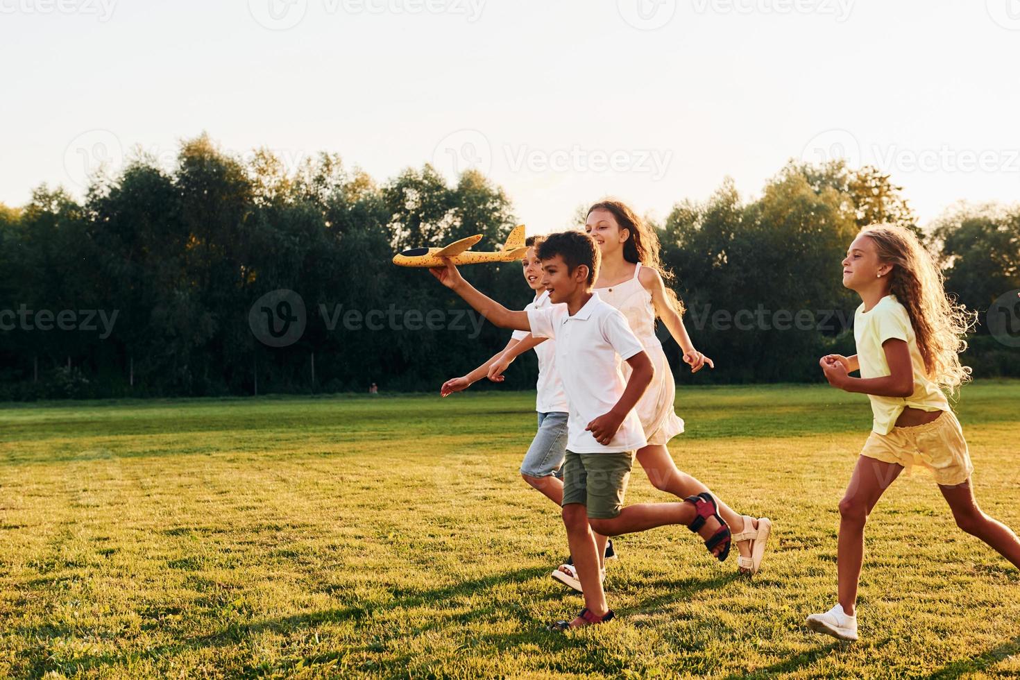 corriendo con avión de juguete. grupo de niños felices está al aire libre en el campo deportivo durante el día foto