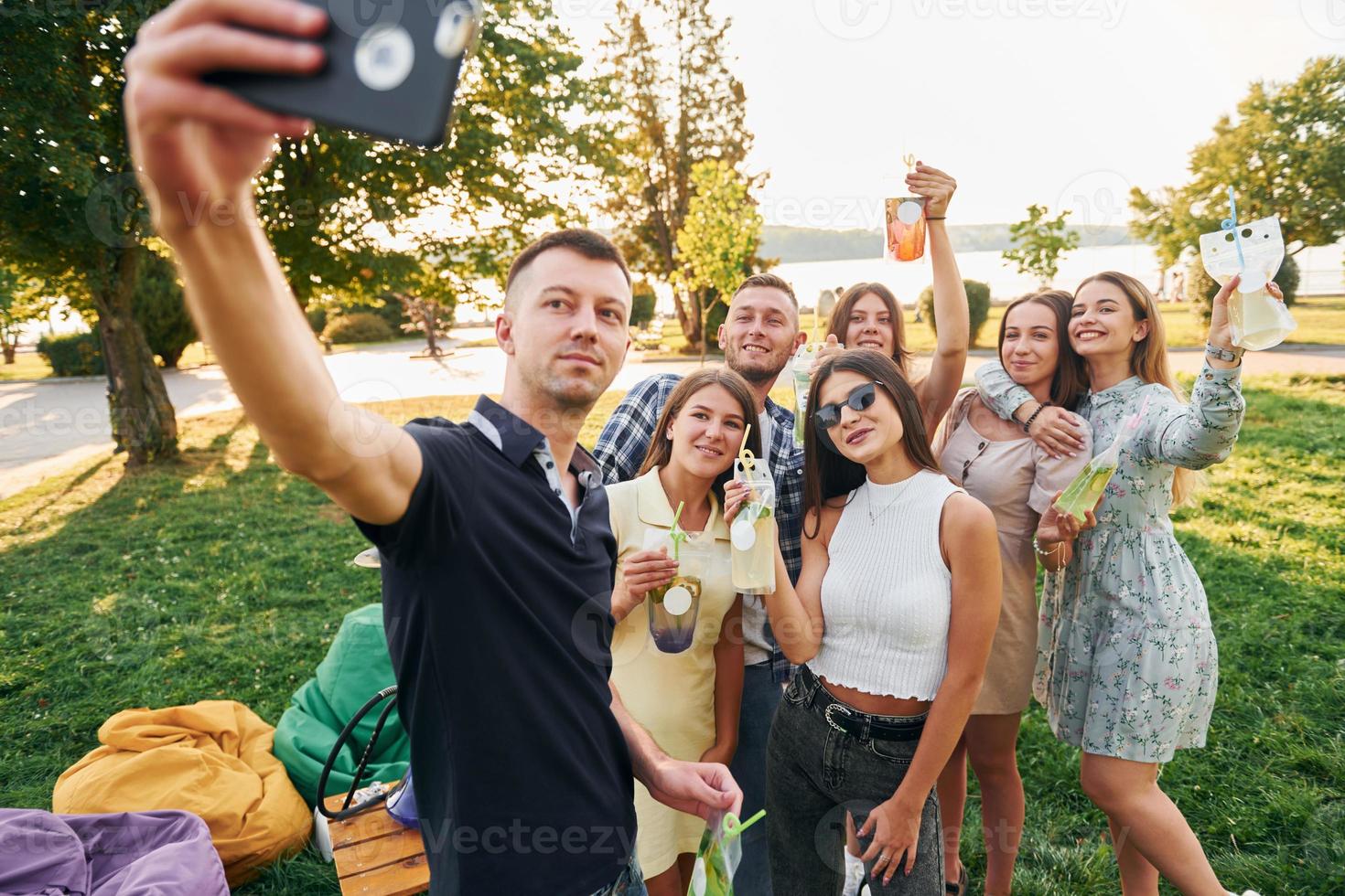 Man taking a selfie. Group of young people have a party in the park at summer daytime photo