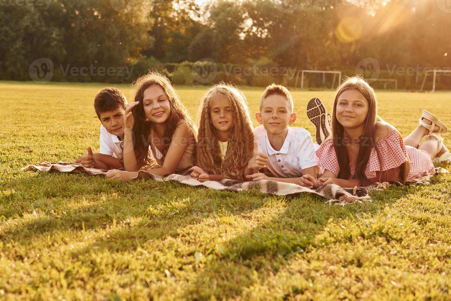 Front view. Group of happy kids is outdoors on the sportive field at daytime photo