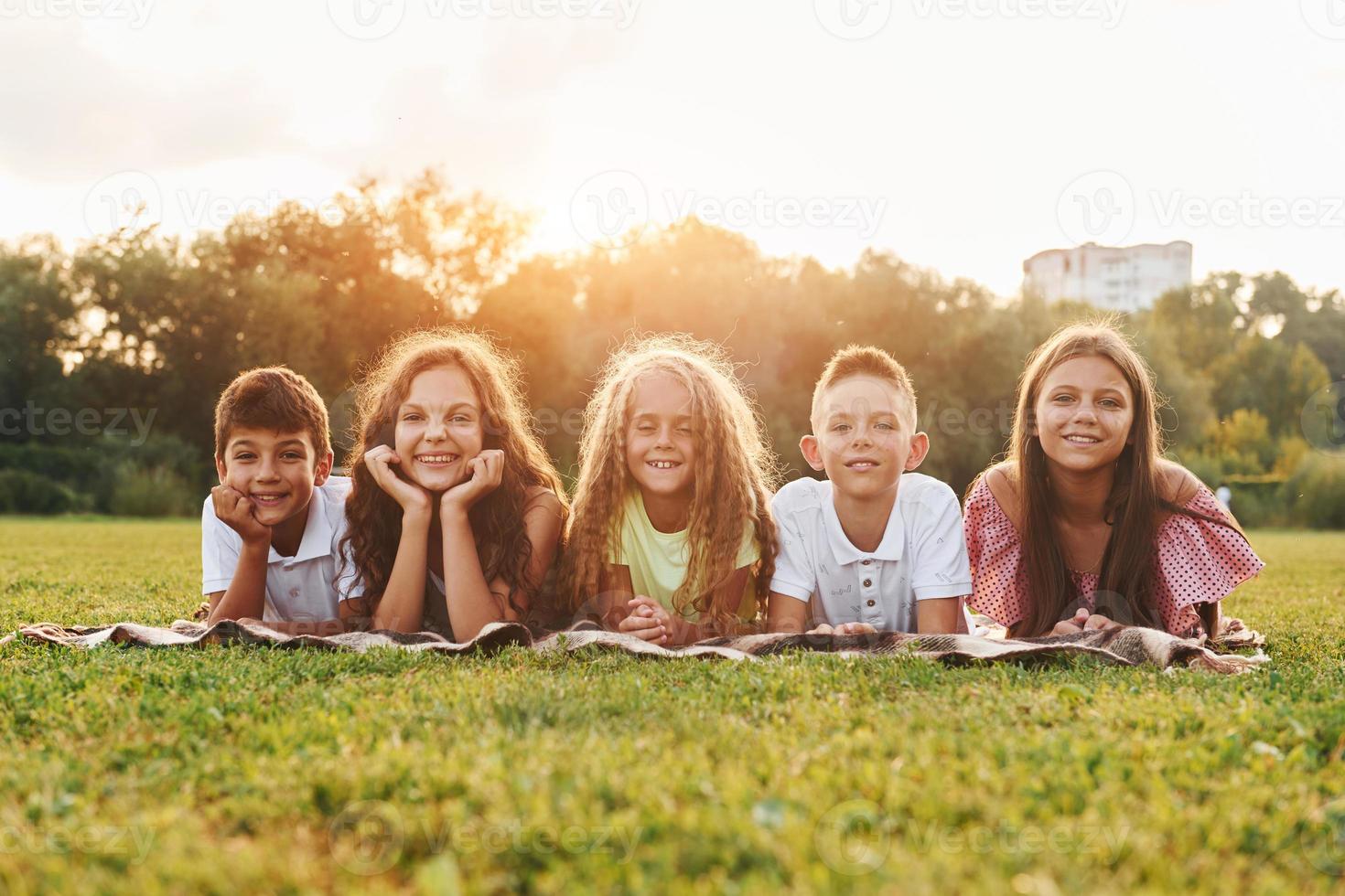 Front view. Group of happy kids is outdoors on the sportive field at daytime photo