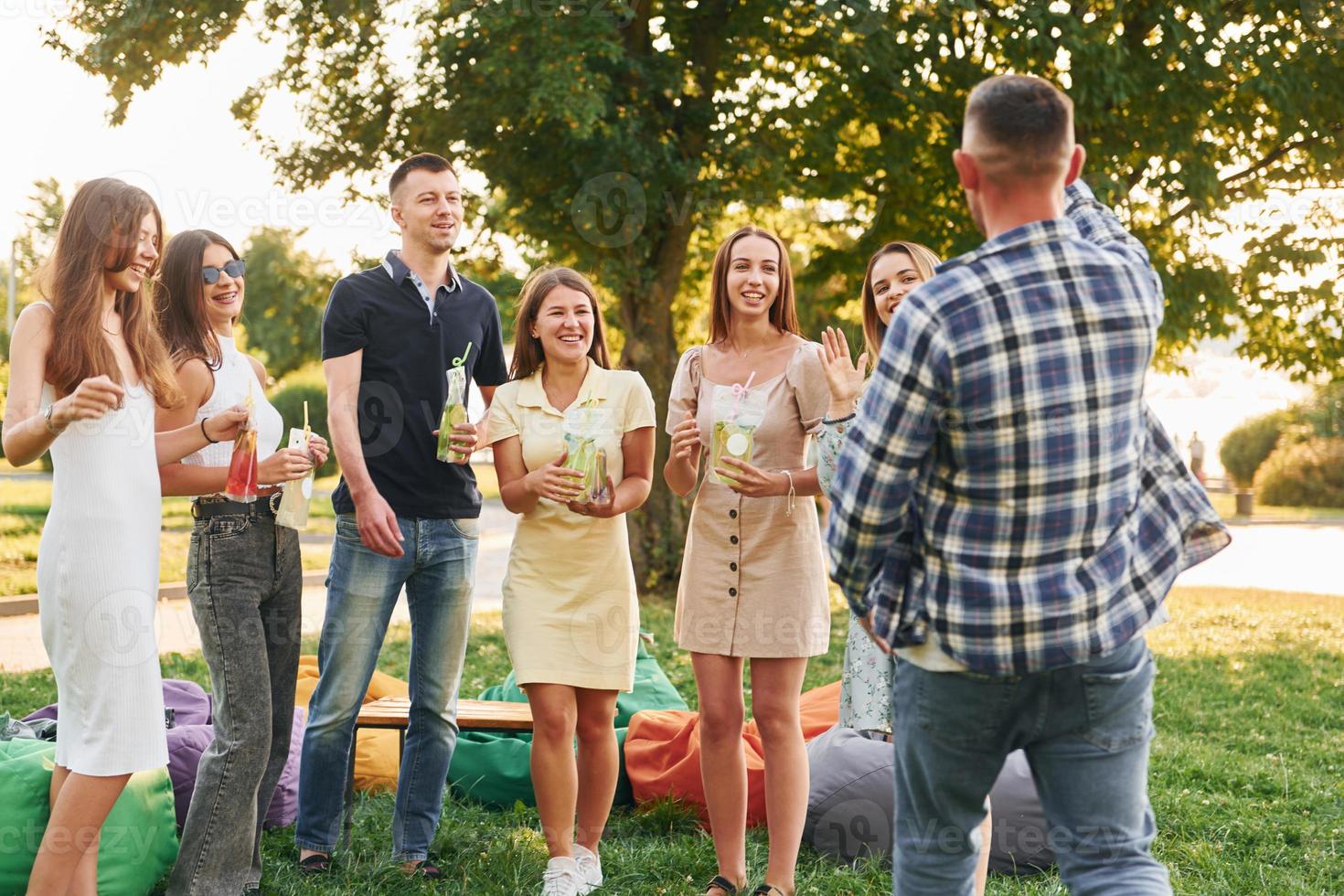 Standing with cocktails. Group of young people have a party in the park at summer daytime photo