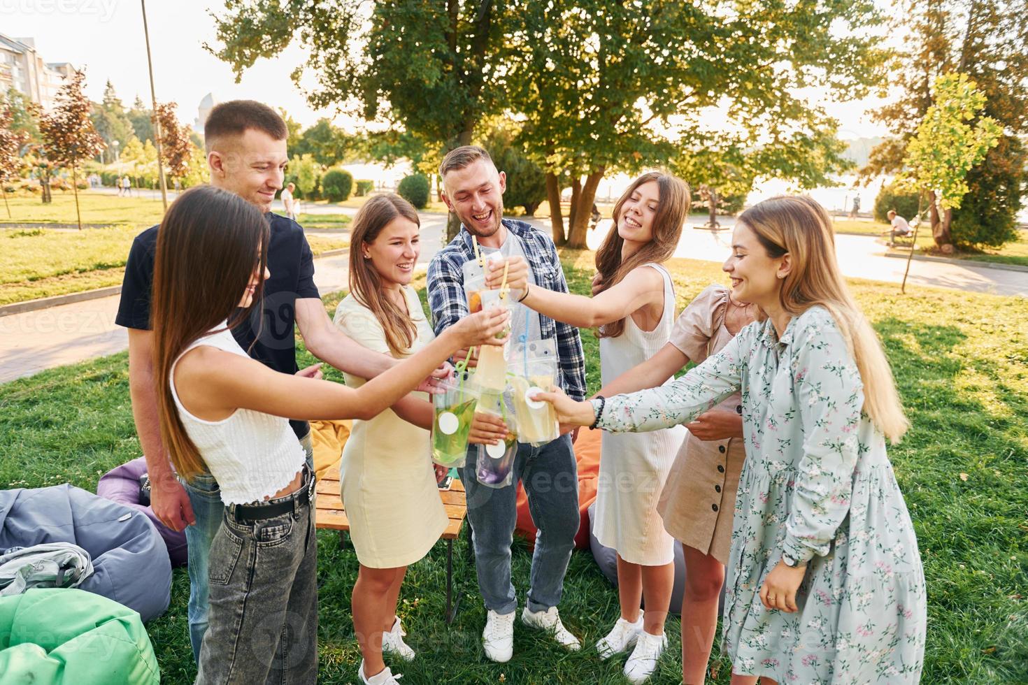 Having a drink. Group of young people have a party in the park at summer daytime photo