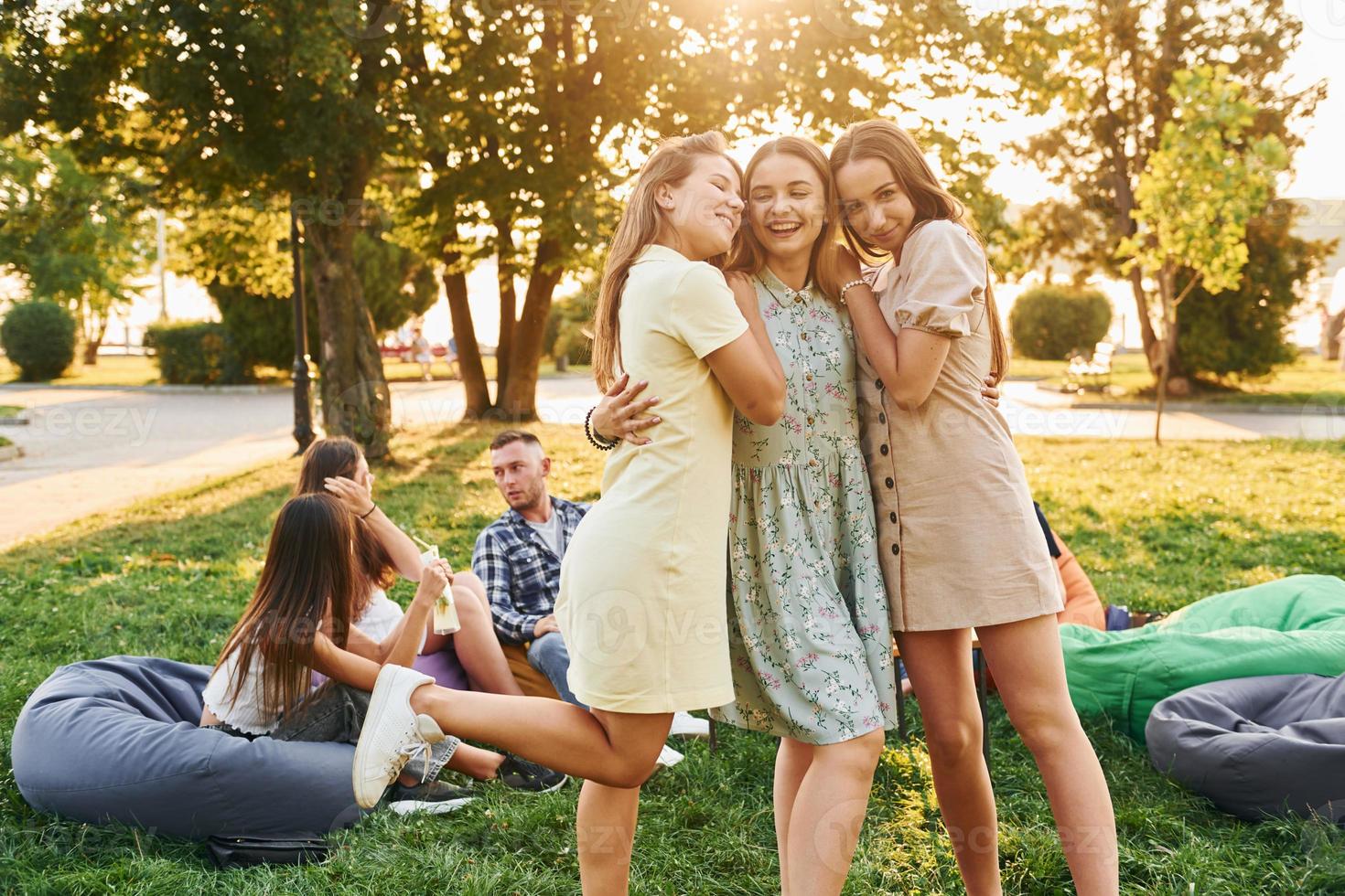 Women embracing each other. Group of young people have a party in the park at summer daytime photo