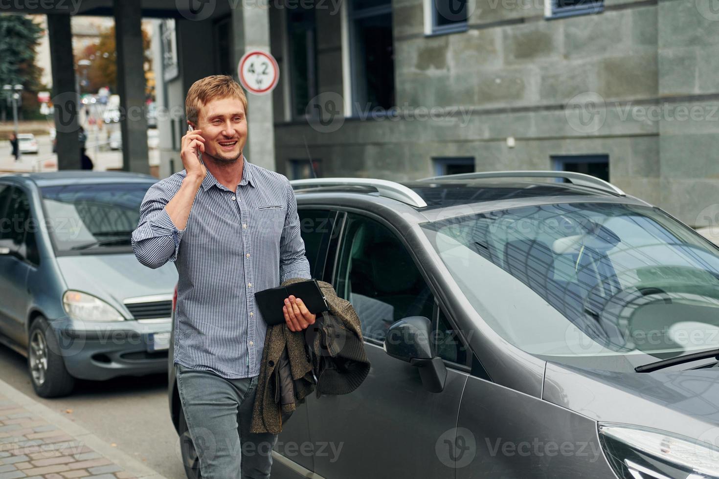 Talking by phone. Man having a walk outdoors in the city at daytime photo
