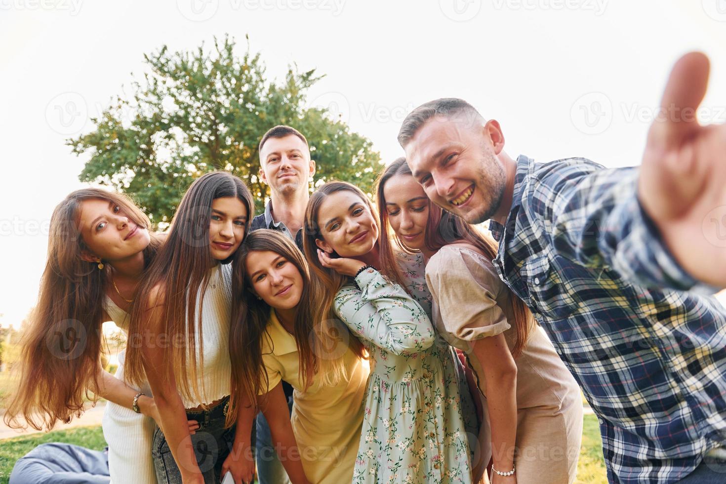 tomando una autofoto. grupo de jóvenes tienen una fiesta en el parque durante el día de verano foto