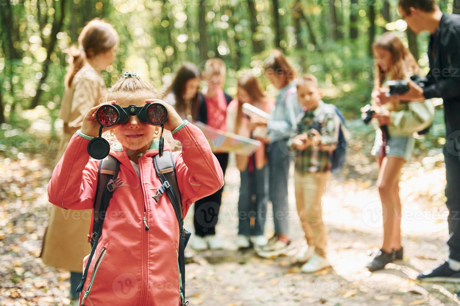 Girl looking into binoculars. Kids in green forest at summer daytime together photo