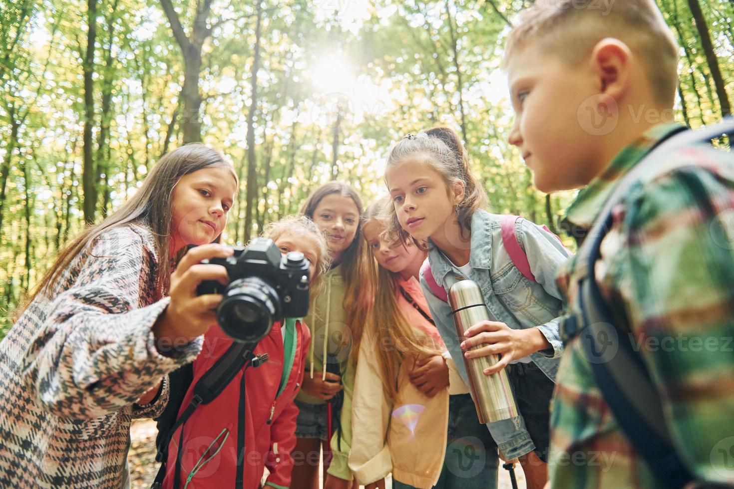 Holding camera. Kids in green forest at summer daytime together photo
