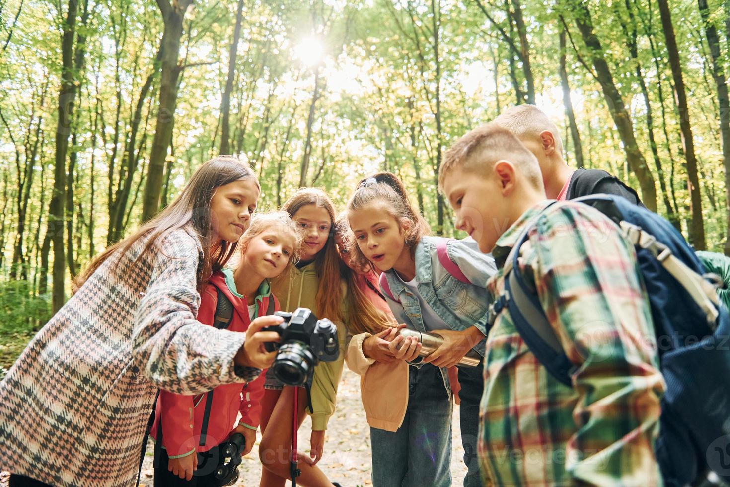 Holding camera. Kids in green forest at summer daytime together photo