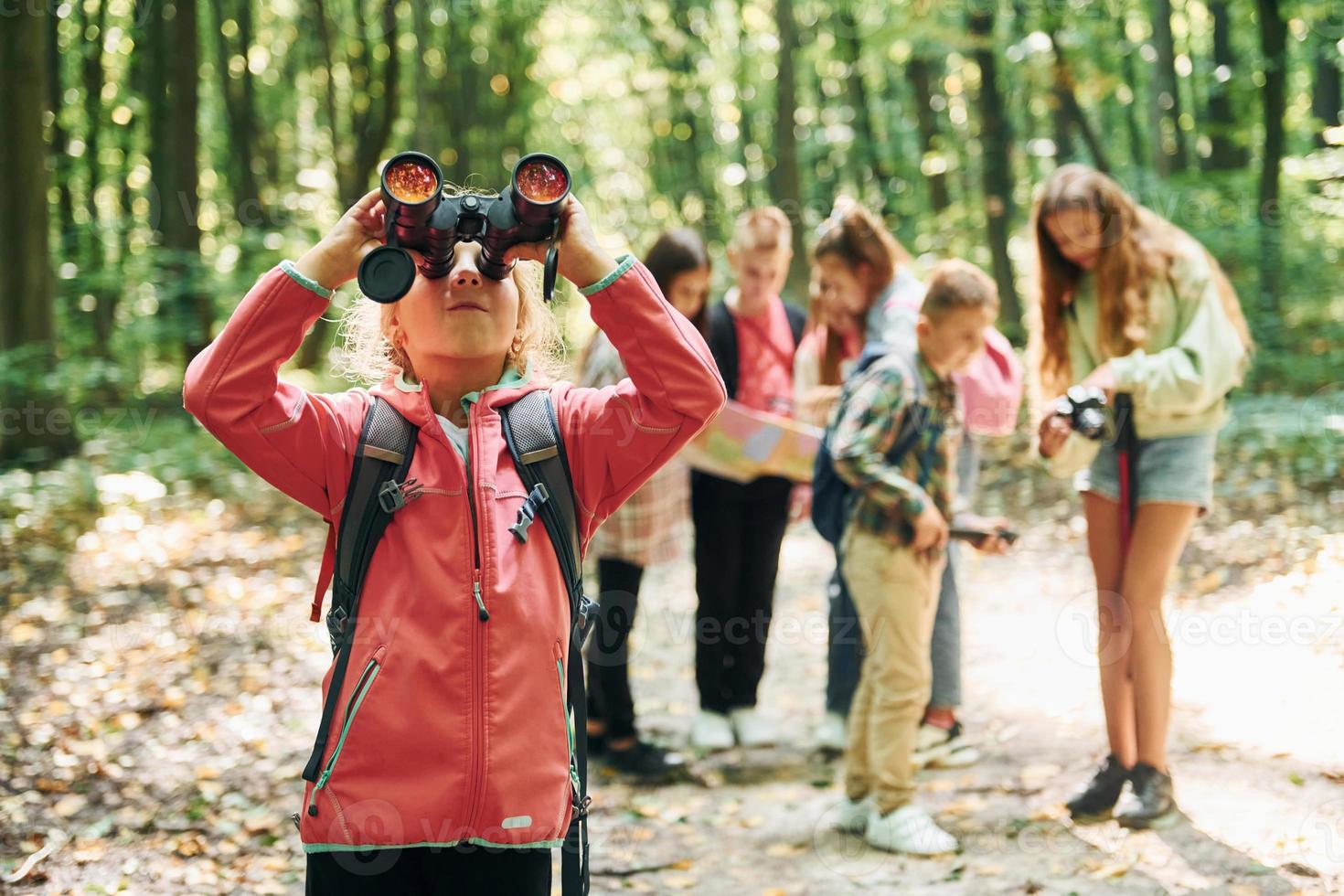 Girl looking into binoculars. Kids in green forest at summer daytime together photo