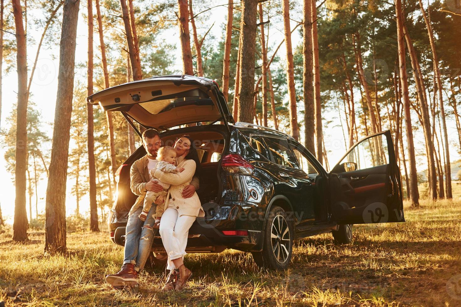 Leaning on the car. Happy family of father, mother and little daughter is in the forest photo