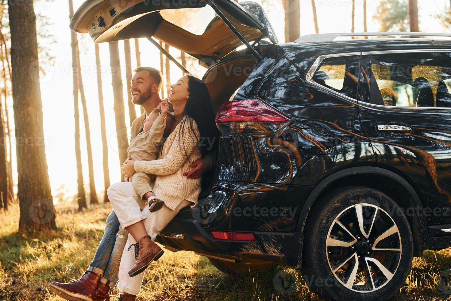 With black colored automobile. Happy family of father, mother and little daughter is in the forest photo