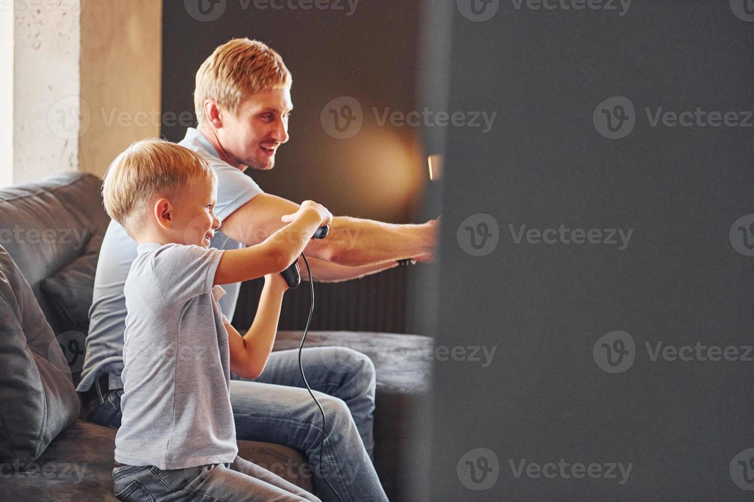 Holding video game controllers. Father and son is indoors at home together photo