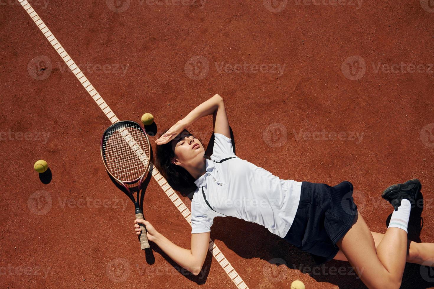 Tired, laying down. Female tennis player is on the court at daytime photo