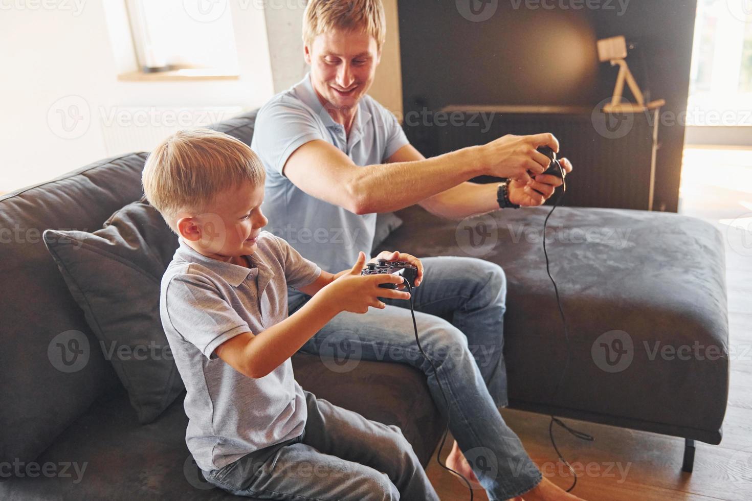 With video game joysticks. Father and son is indoors at home together photo