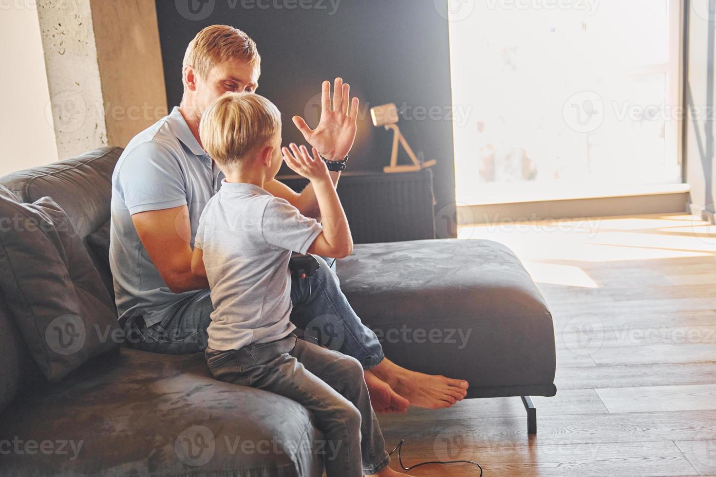 Playing video game. Father and son is indoors at home together photo