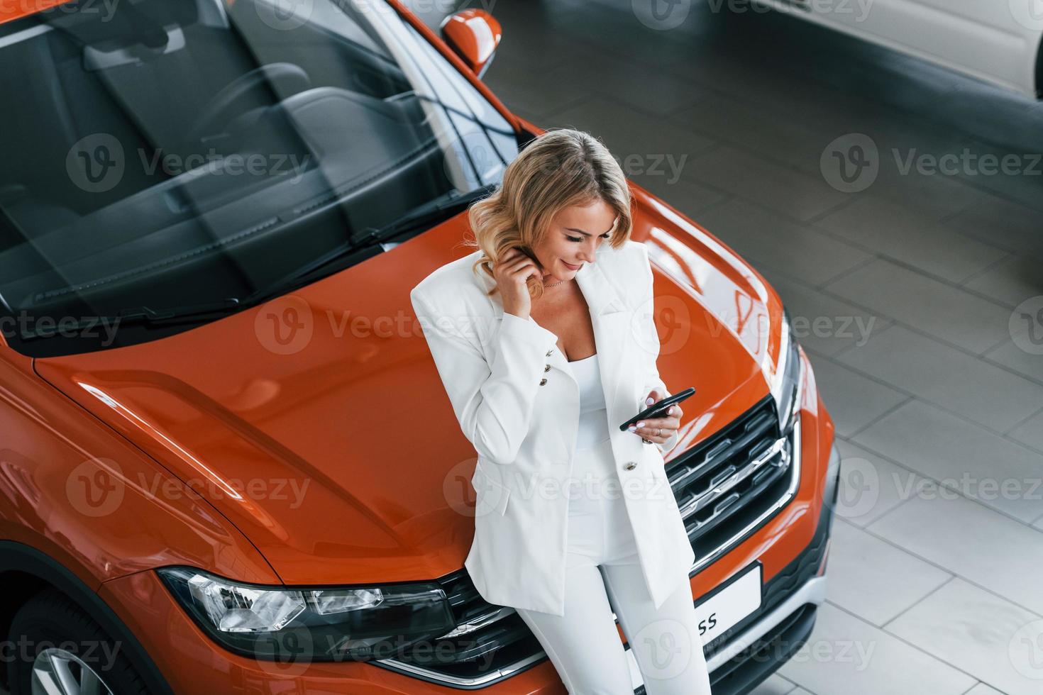 Leaning on the car. Woman in formal clothes is indoors in the autosalon photo