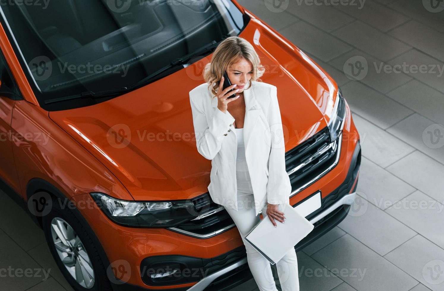 With phone in hand. Woman in formal clothes is indoors in the autosalon photo
