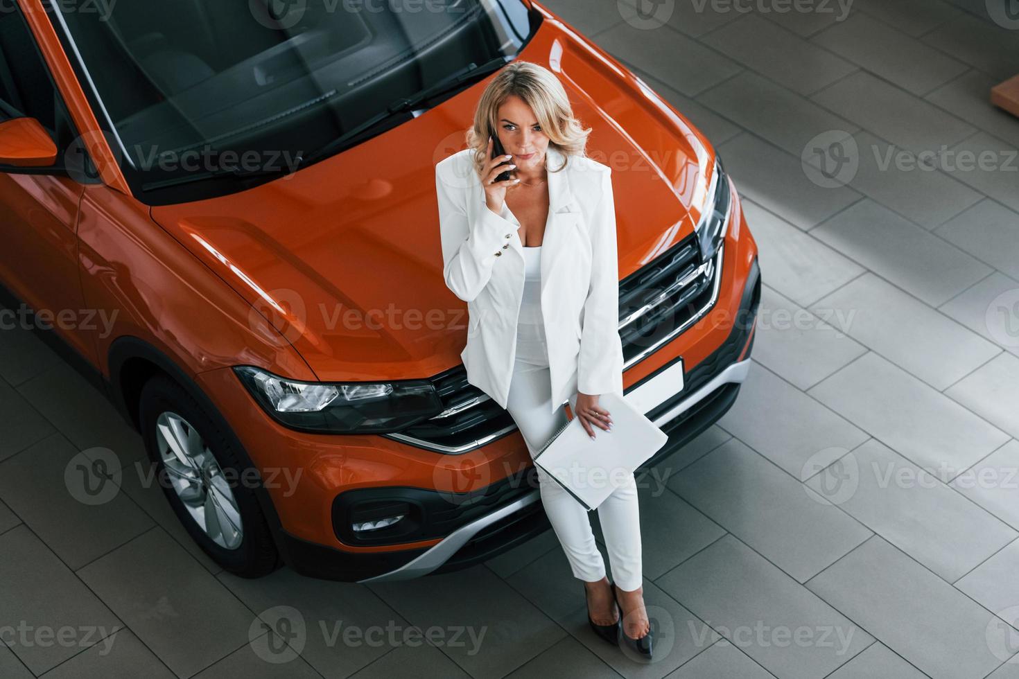 With phone in hand. Woman in formal clothes is indoors in the autosalon photo