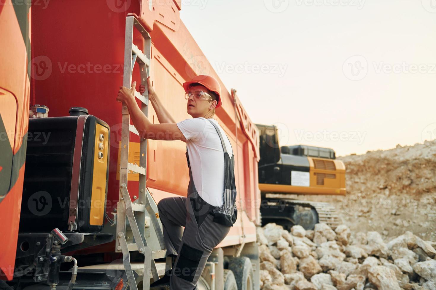 Going up to the vehicle seat. Worker in professional uniform is on the borrow pit at daytime photo