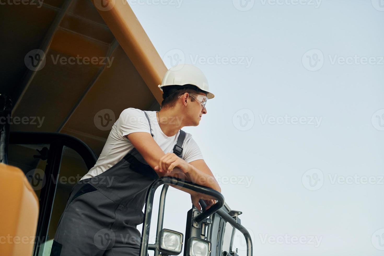 On the vehicle. Worker in professional uniform is on the borrow pit at daytime photo