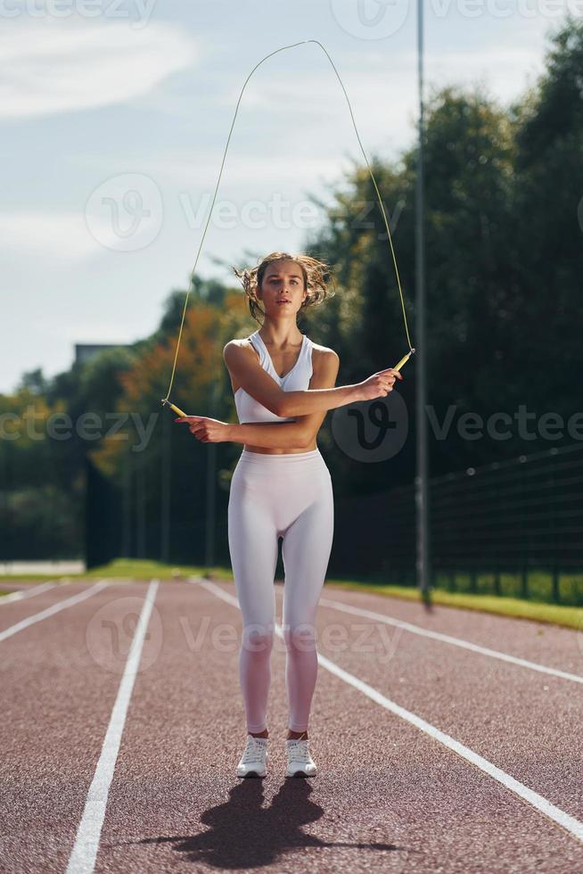 Jumping rope. Young woman in sportive clothes is exercising outdoors photo