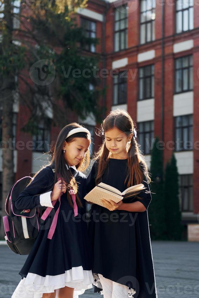 con libros dos colegialas están afuera juntas cerca del edificio de la escuela foto