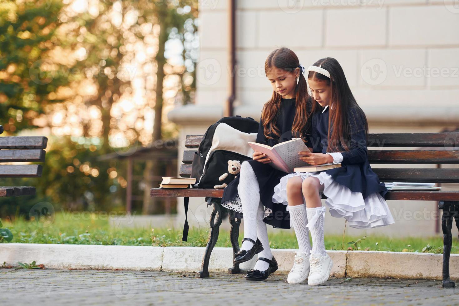 dos colegialas están sentadas afuera juntas cerca del edificio de la escuela foto