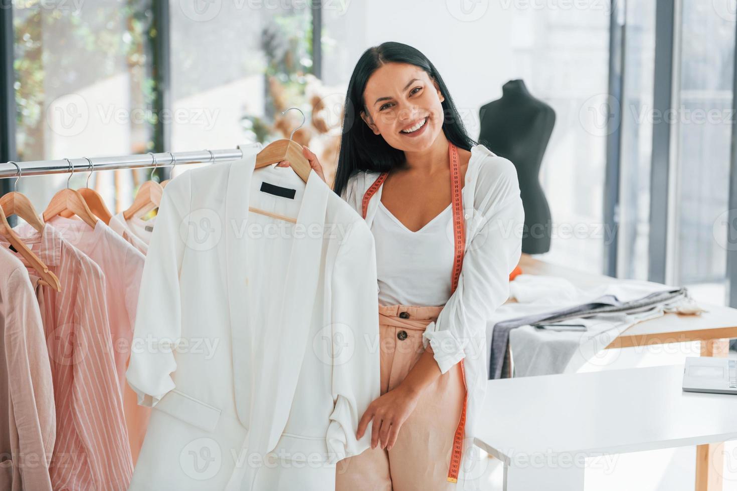 Standing and smiling. Seamstress is in her office that is with different clothes photo