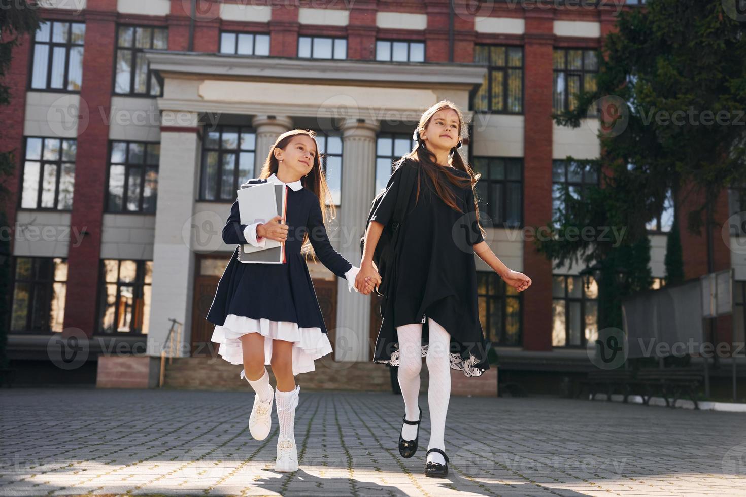 Two schoolgirls is running outside together near school building photo