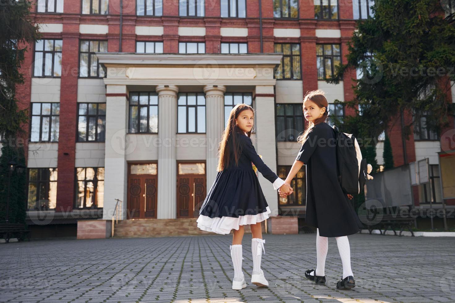 Rear view. Two schoolgirls is outside together near school building photo