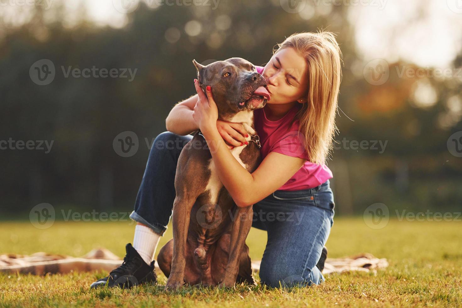 Positive emotions. Woman in casual clothes is with pit bull outdoors photo