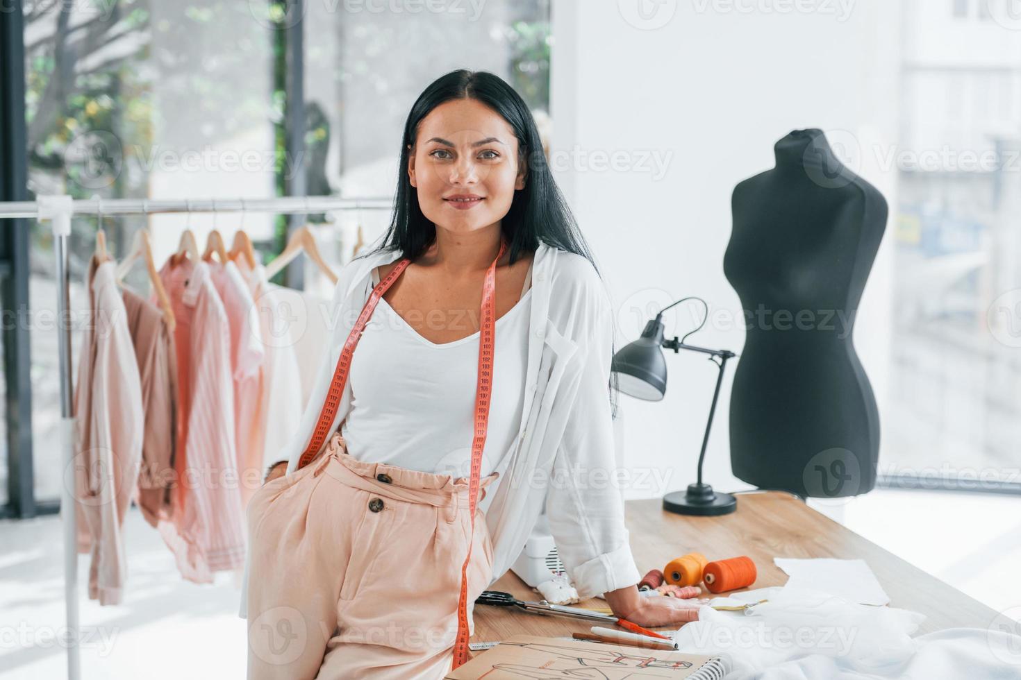 Standing by the table. Seamstress is in her office that is with different clothes photo