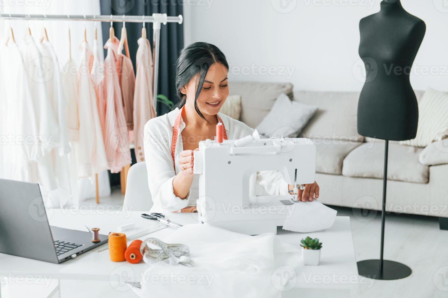 máquina de coser de color blanco. la costurera está en su oficina que está con ropa diferente foto