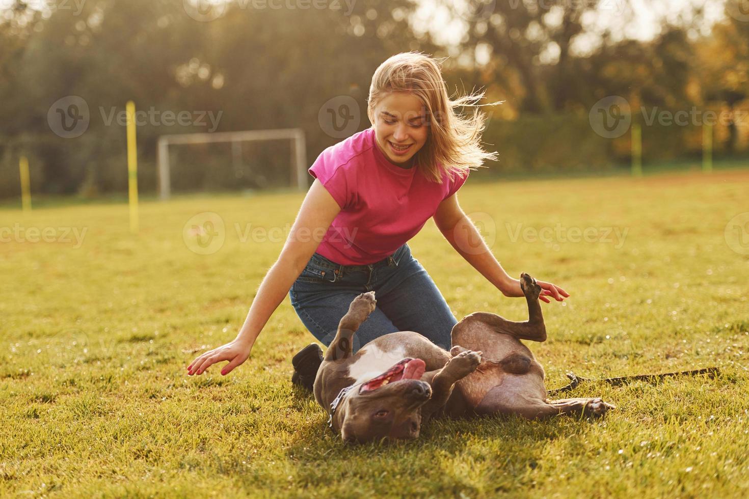 Playing on the ground. Woman in casual clothes is with pit bull outdoors photo