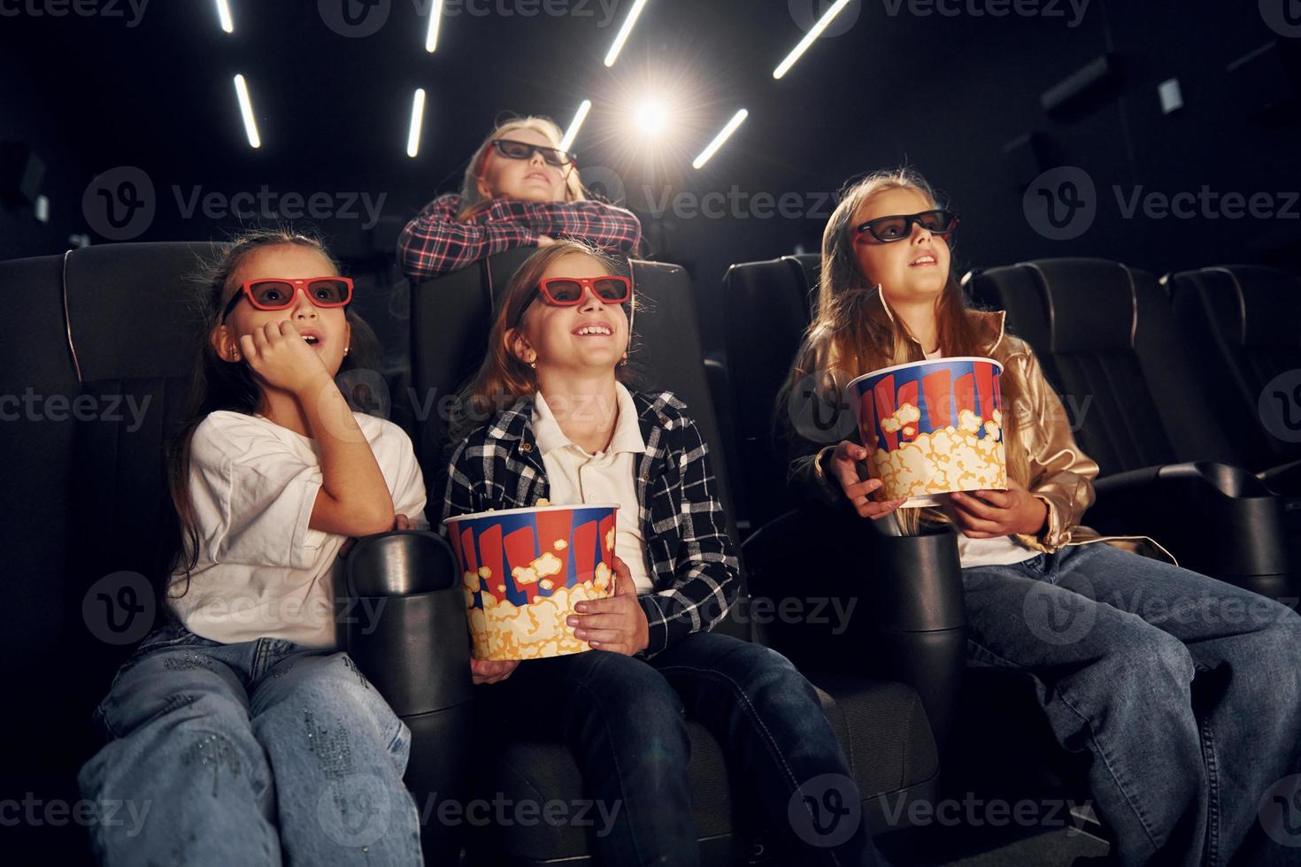 With popcorn. Group of kids sitting in cinema and watching movie together photo