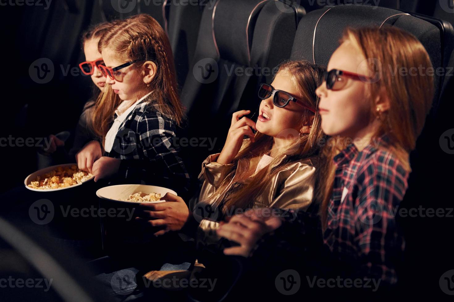 Delicious popcorn. Group of kids sitting in cinema and watching movie together photo