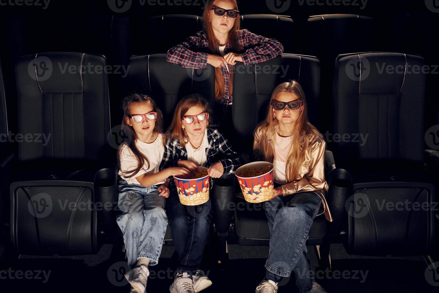 Front view. Group of kids sitting in cinema and watching movie together photo