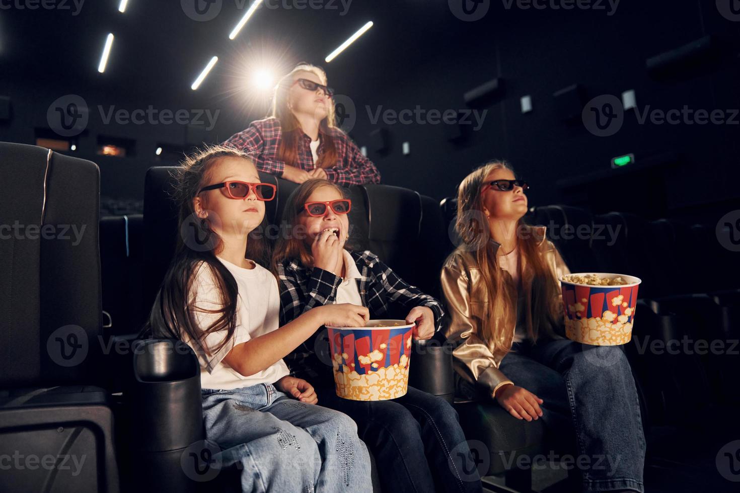 Eating popcorn. Group of kids sitting in cinema and watching movie together photo