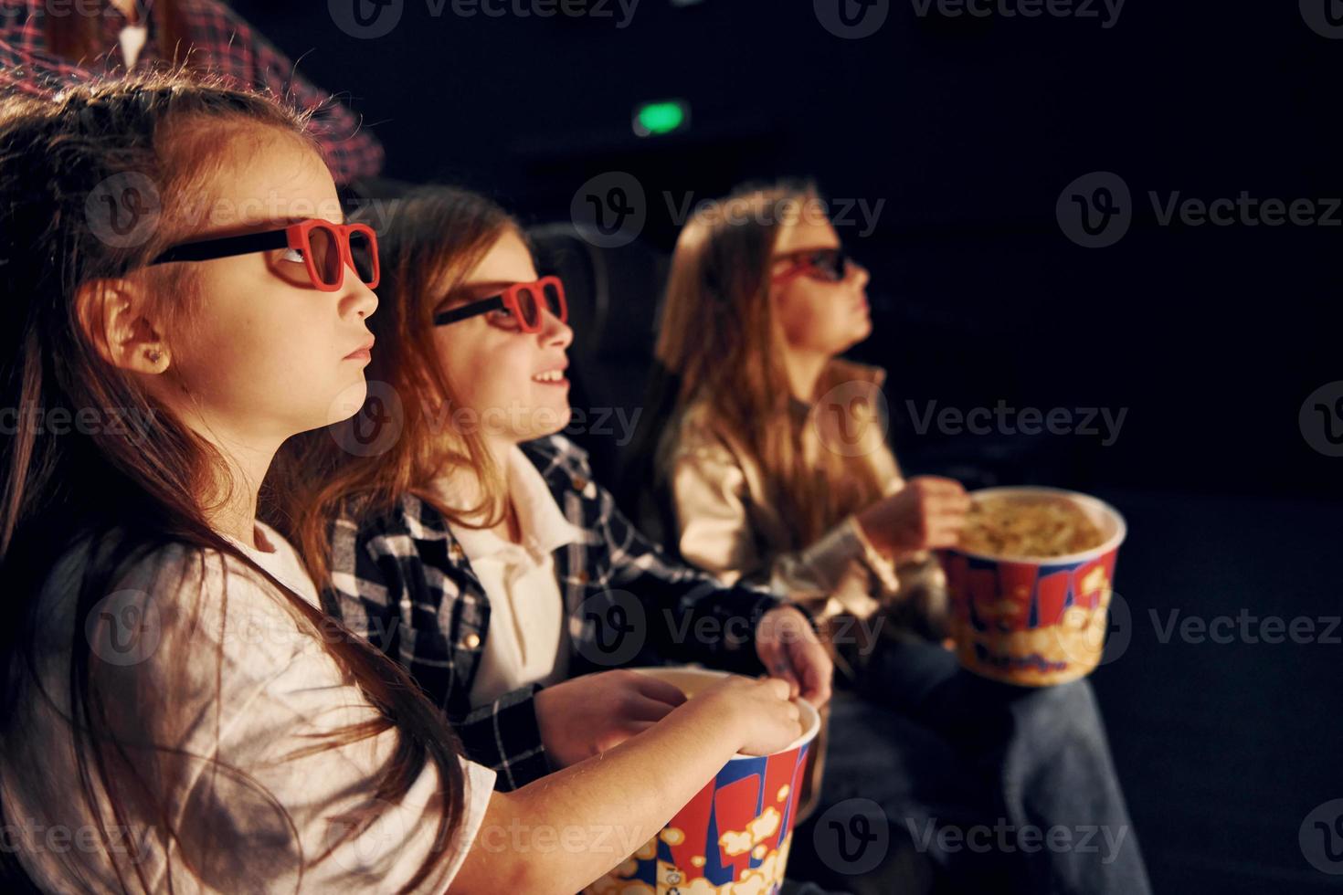 Eating popcorn. Group of kids sitting in cinema and watching movie together photo
