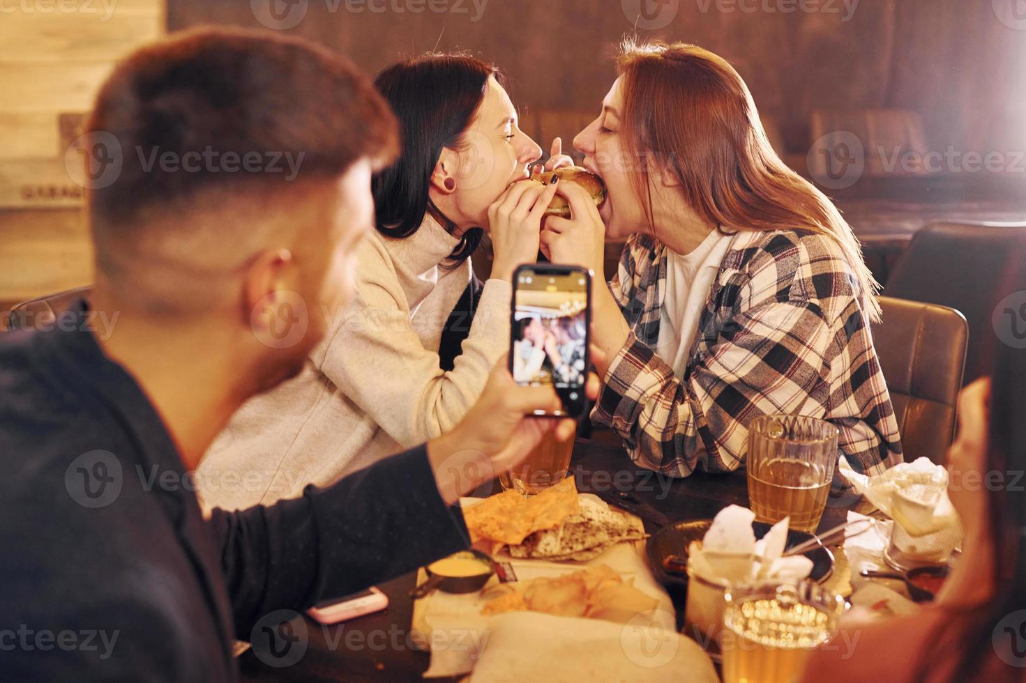 Eating food. Group of young friends sitting together in bar with beer photo