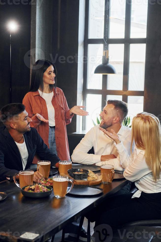 Eating food. Group of young friends sitting together in bar with beer photo