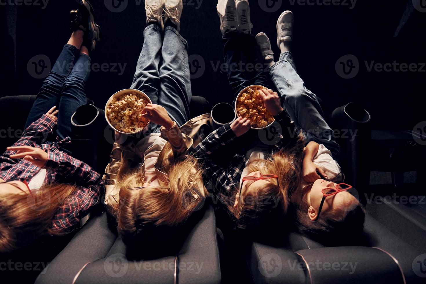 Delicious popcorn. Group of kids sitting in cinema and watching movie together photo