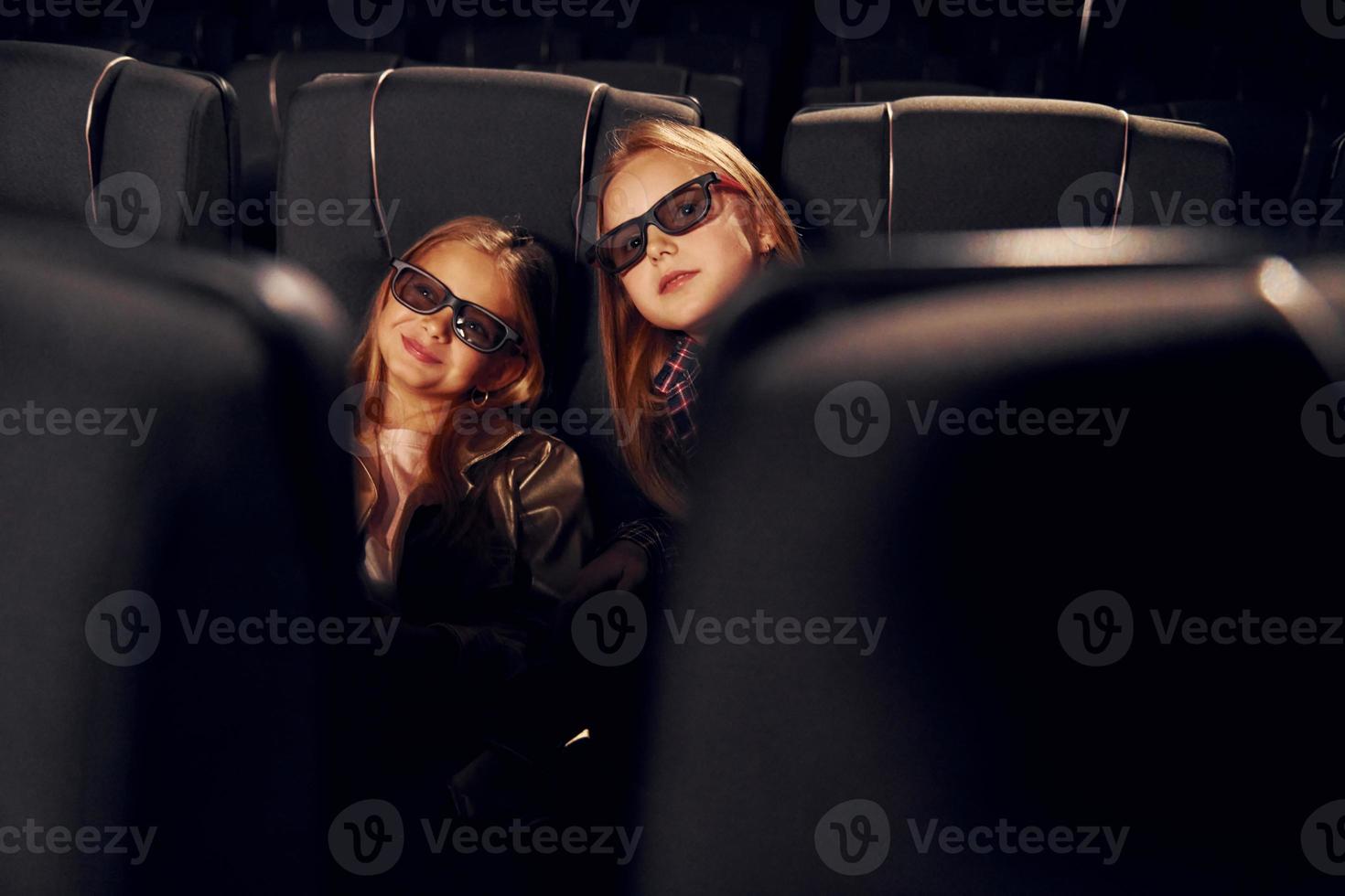 Two kids sitting in cinema and watching movie together photo
