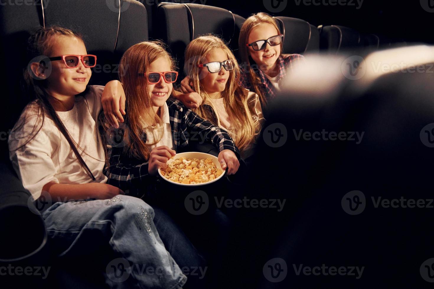 Weekend fun. Group of kids sitting in cinema and watching movie together photo