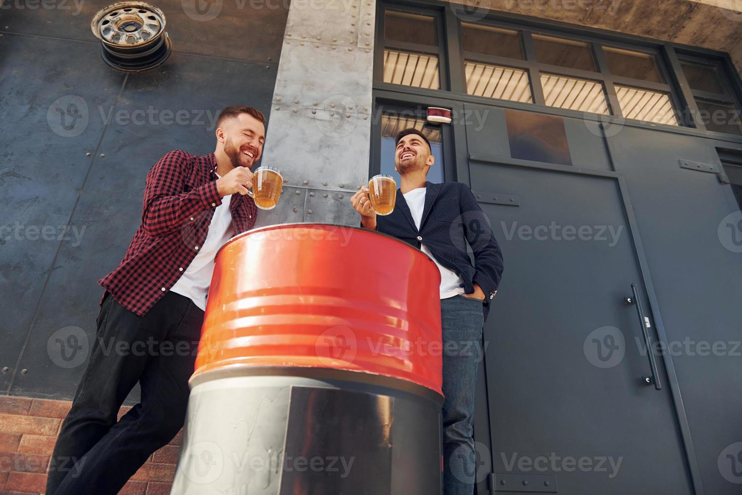 Two friends standing outdoors and holding glasses with beer photo