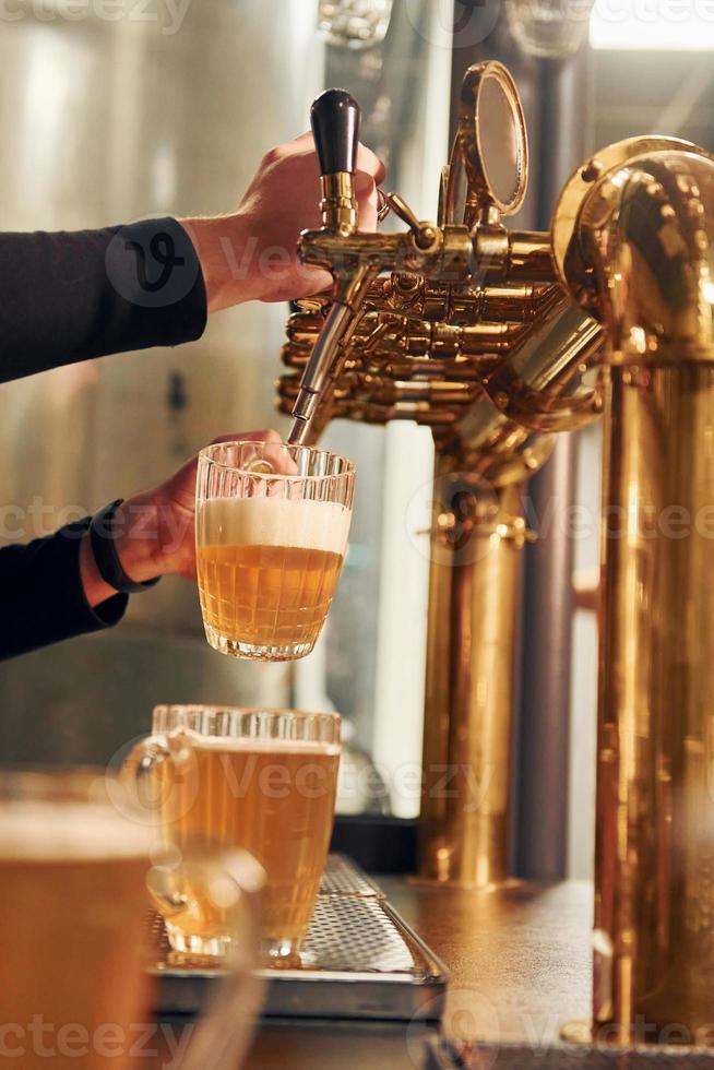 Side view of man's hands that fills glasses by beer photo