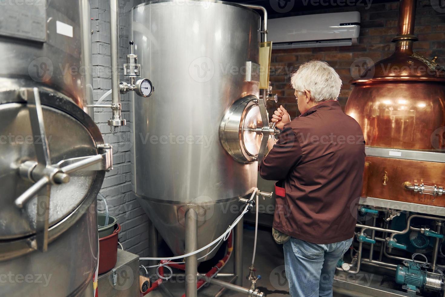 estilo retro. el anciano está parado en el almacenamiento con equipo para cerveza foto